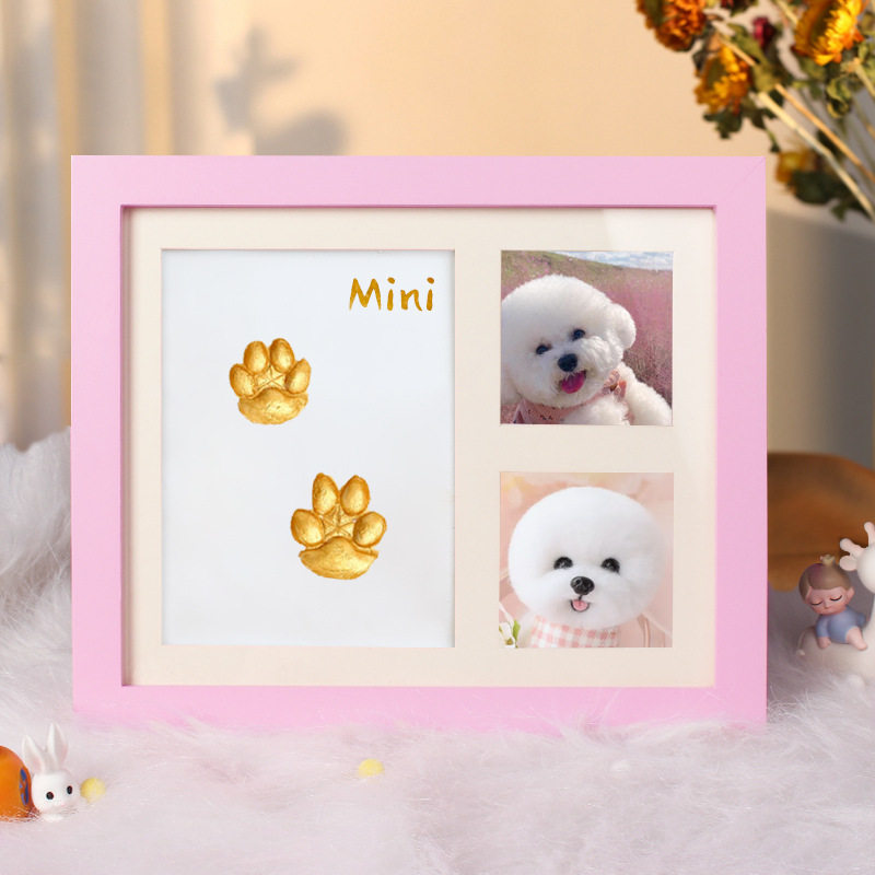 Pink photo frame with paw prints and a small dog inside, on a soft surface with flowers in the background.