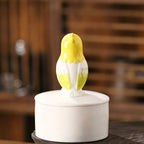 Yellow and white ceramic parakeet on a white base against a blurred wooden background