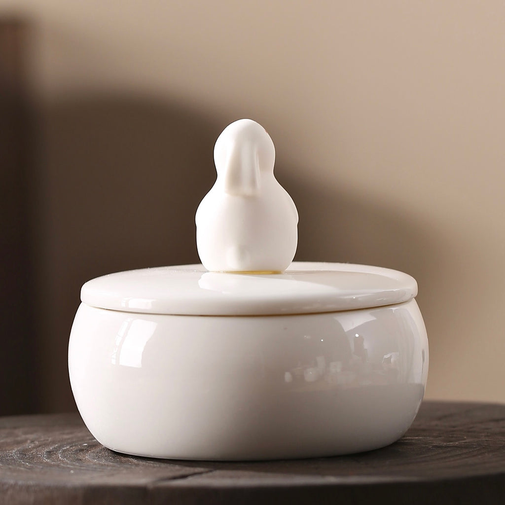 White ceramic jar with a bird-shaped lid on a wooden surface.