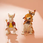 Two figurines of a rabbit and a lion with crowns and scepters on a pink background