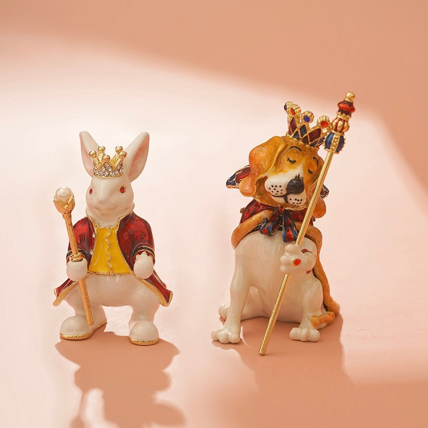 Two figurines of a rabbit and a lion with crowns and scepters on a pink background