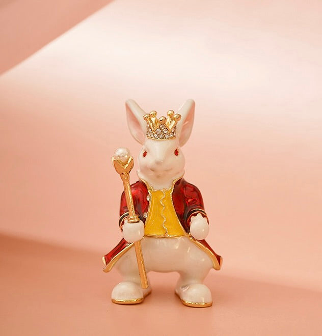 Decorative figurine of a rabbit king with a crown, scepter, and red robe on a pink background