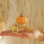 Decorative pumpkin with a gold carriage on a hand against a neutral background