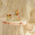 Two decorative animal figurines on a small white plate held by a person.