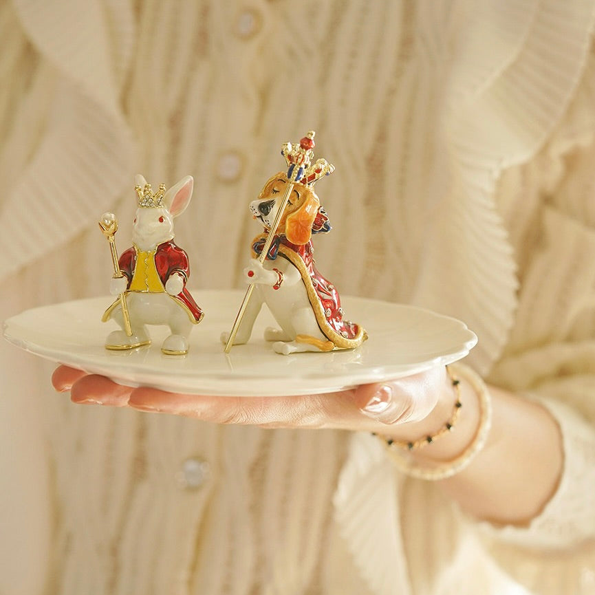 Two decorative animal figurines on a small white plate held by a person.
