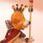 Decorative figurine of a dog wearing a crown and holding a scepter on a light pink background