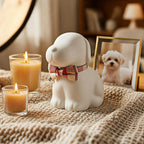Dog-shaped candle holder with two lit candles on a textured surface, with a framed photo of a dog in the background.