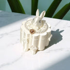 Decorative white rabbit figurine on a matching stand with a heart pendant, set against a light background.