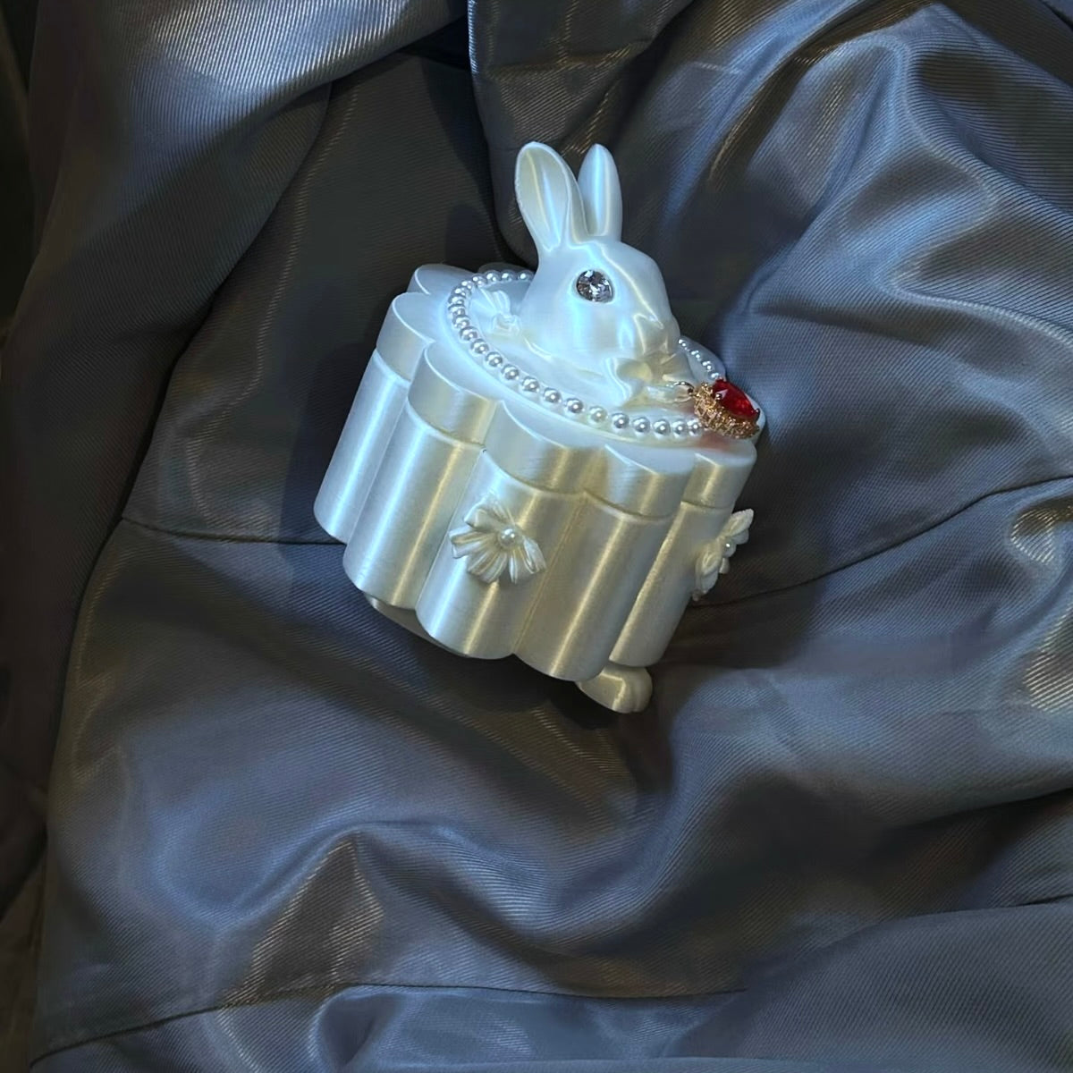 Decorative rabbit-shaped jewelry box with pearls and gemstones on a dark fabric background