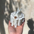 White rabbit figurine on a decorative stand held in a hand with a neutral background