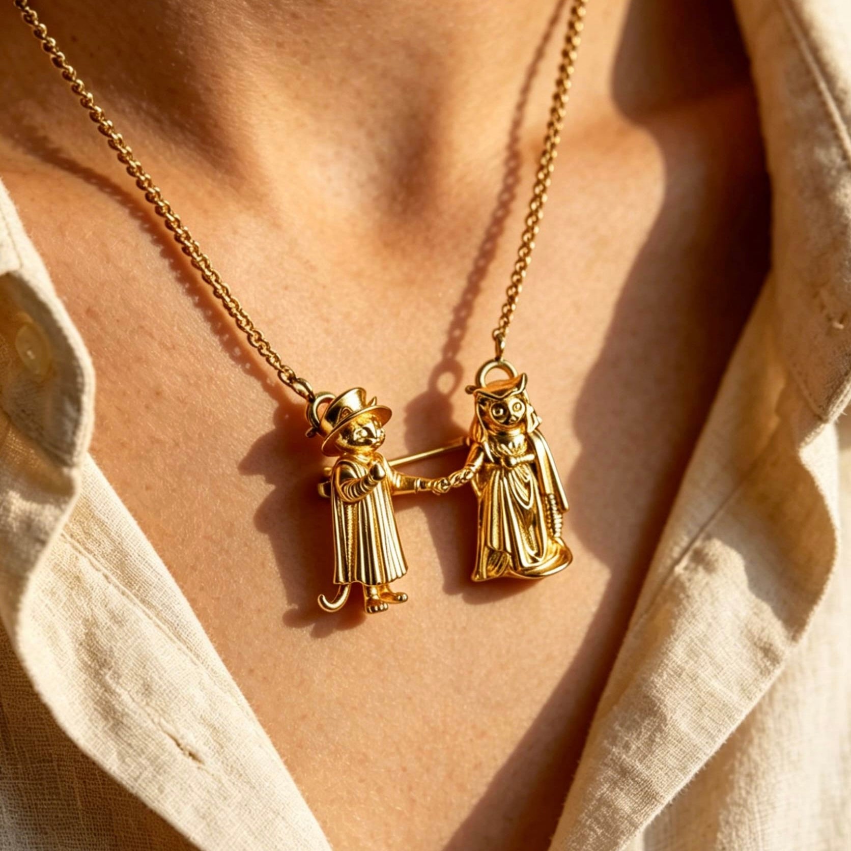 Gold necklace with two small figures on a person wearing a light-colored shirt.