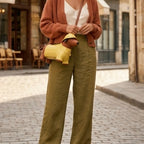 Person wearing a brown cardigan, white top, and green pants with a yellow bag on a street.