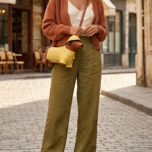 Person wearing a brown cardigan, white top, and green pants with a yellow bag on a street.
