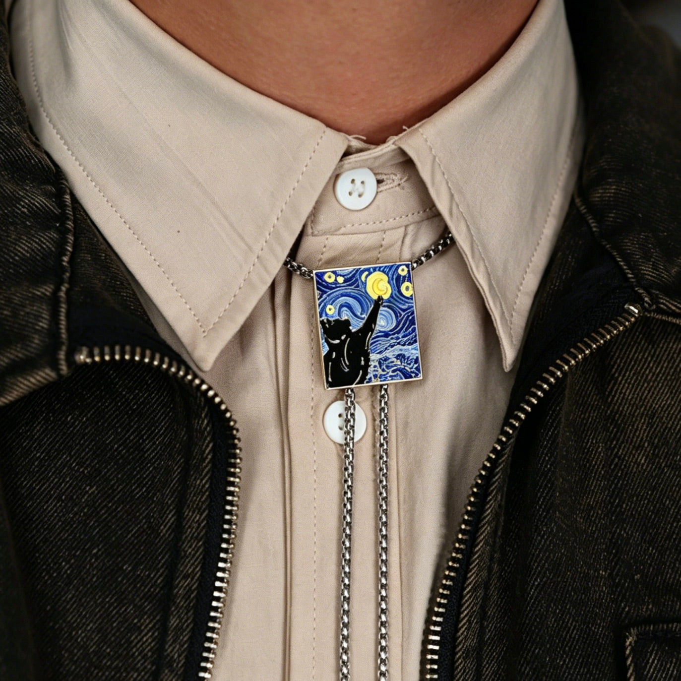 Person wearing a brooch with a black cat design on a beige shirt and dark jacket.