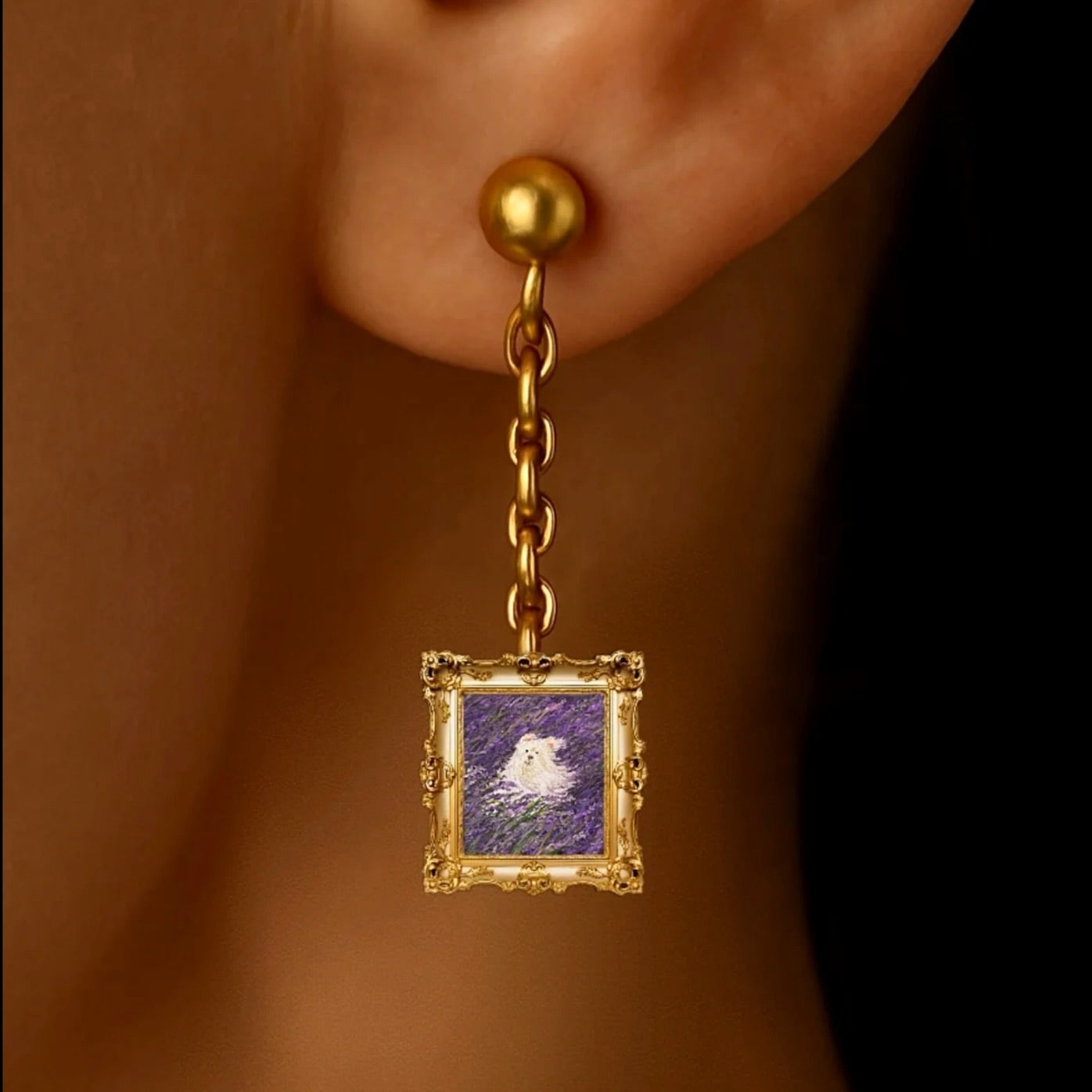 Gold earring with a small framed picture hanging from an earlobe.