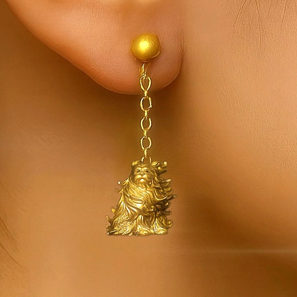 Gold earring with a lion-like figure worn on an ear against a beige background