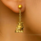 Gold earring with a lion-like figure worn on an ear against a beige background