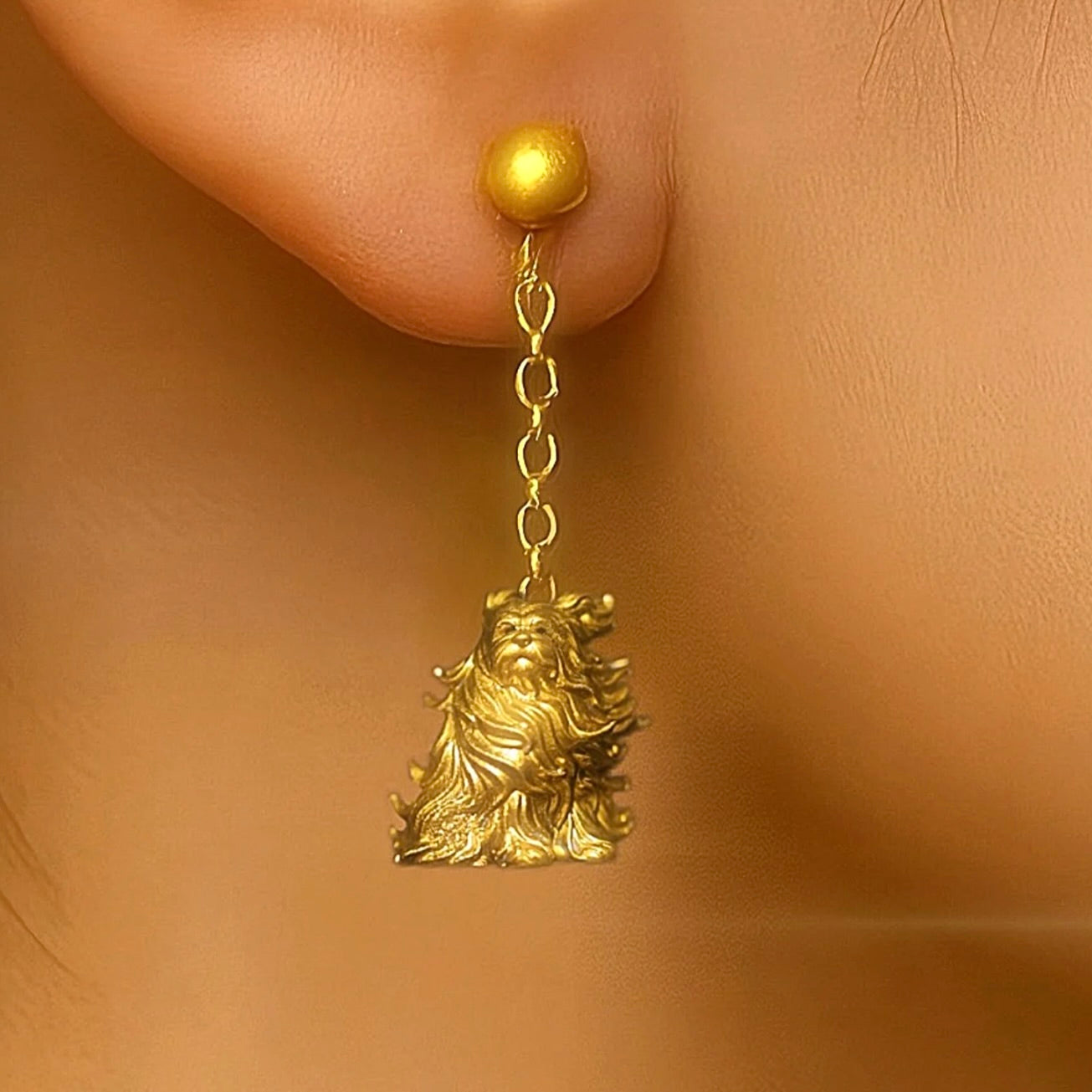 Gold earring with a lion-like figure worn on an ear against a beige background