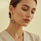 Close-up of a woman wearing a gold earring with a blue gemstone on a beige background