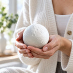A person warmly holding a white cratered moon-shaped biodegradable pet urn in both hands.
