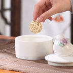 Hand placing a small woven bird toy into an open ceramic bird memorial keepsake box