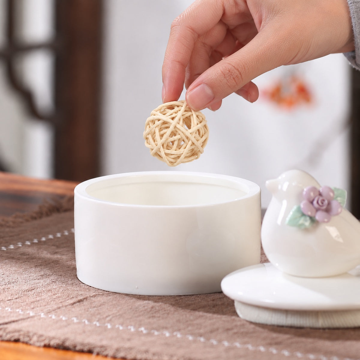 Hand placing a small woven bird toy into an open ceramic bird memorial keepsake box