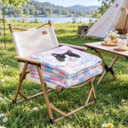 Folded pink and blue cat portrait blanket on a camping chair beside a tent and lake