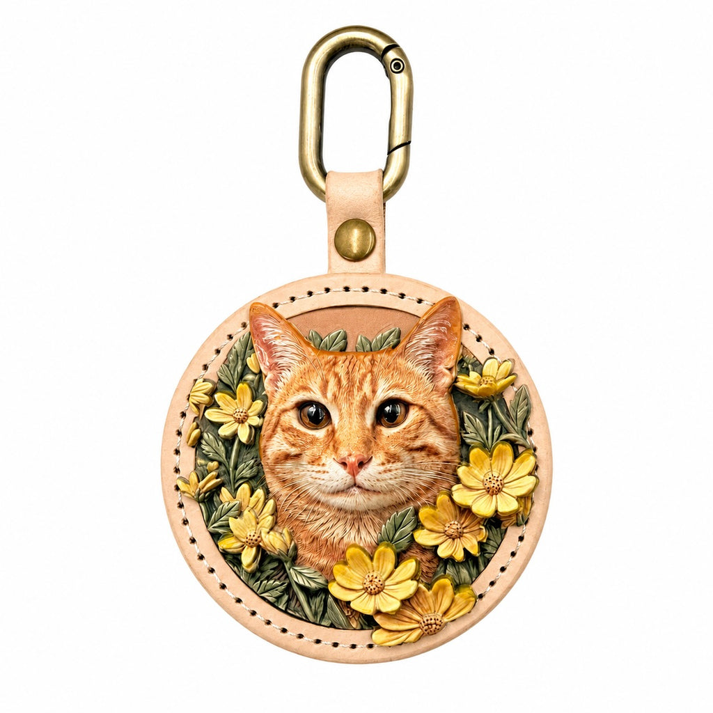 A round stitched leather keychain featuring a custom 3D relief portrait of an orange tabby cat, intricately hand-painted and framed by yellow flowers. Attached to a gold metal clasp, this personalized pet charm by Memopaw serves as a unique handmade pet memorial gift.