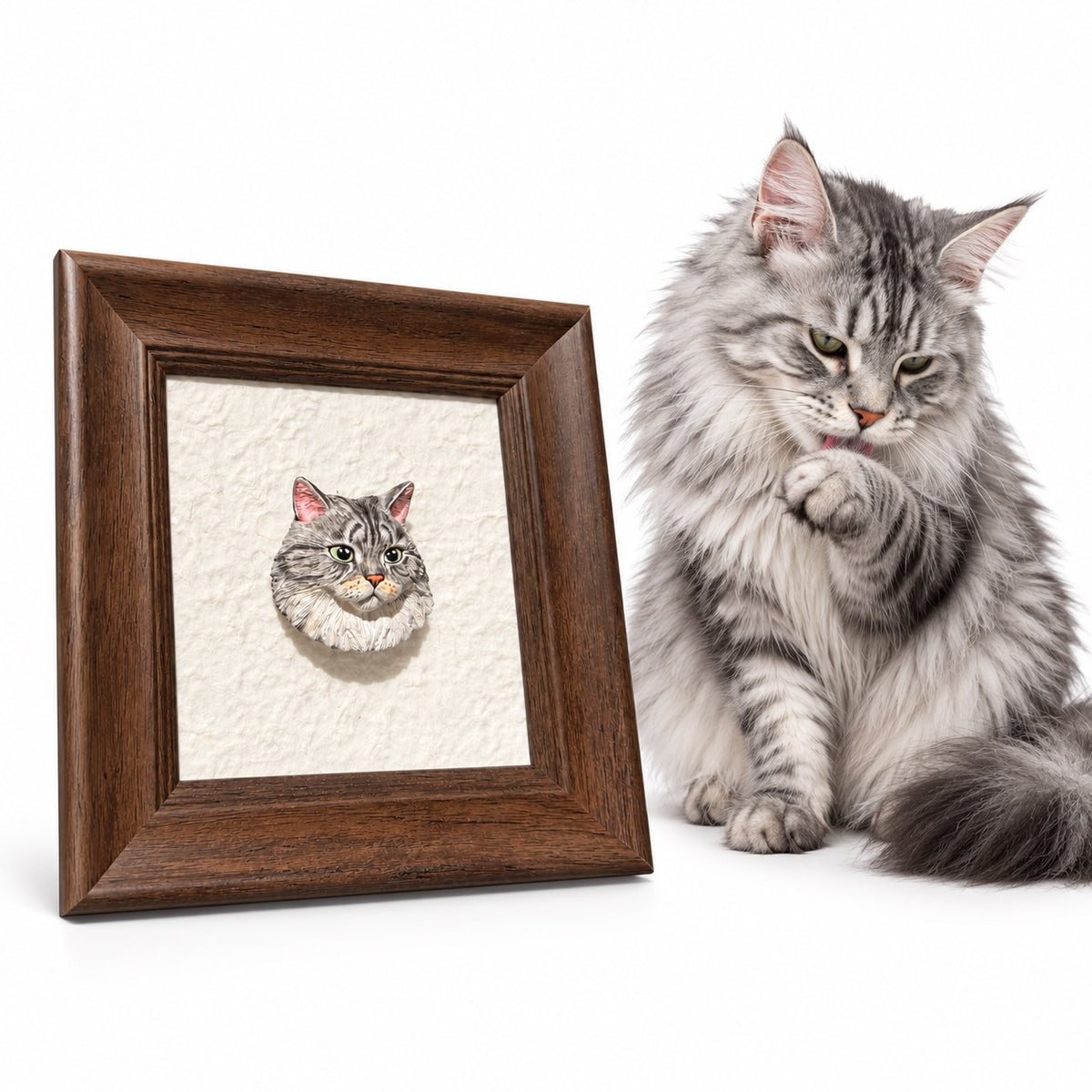 Gray tabby cat beside a brown frame displaying a raised cat head portrait on a cream background