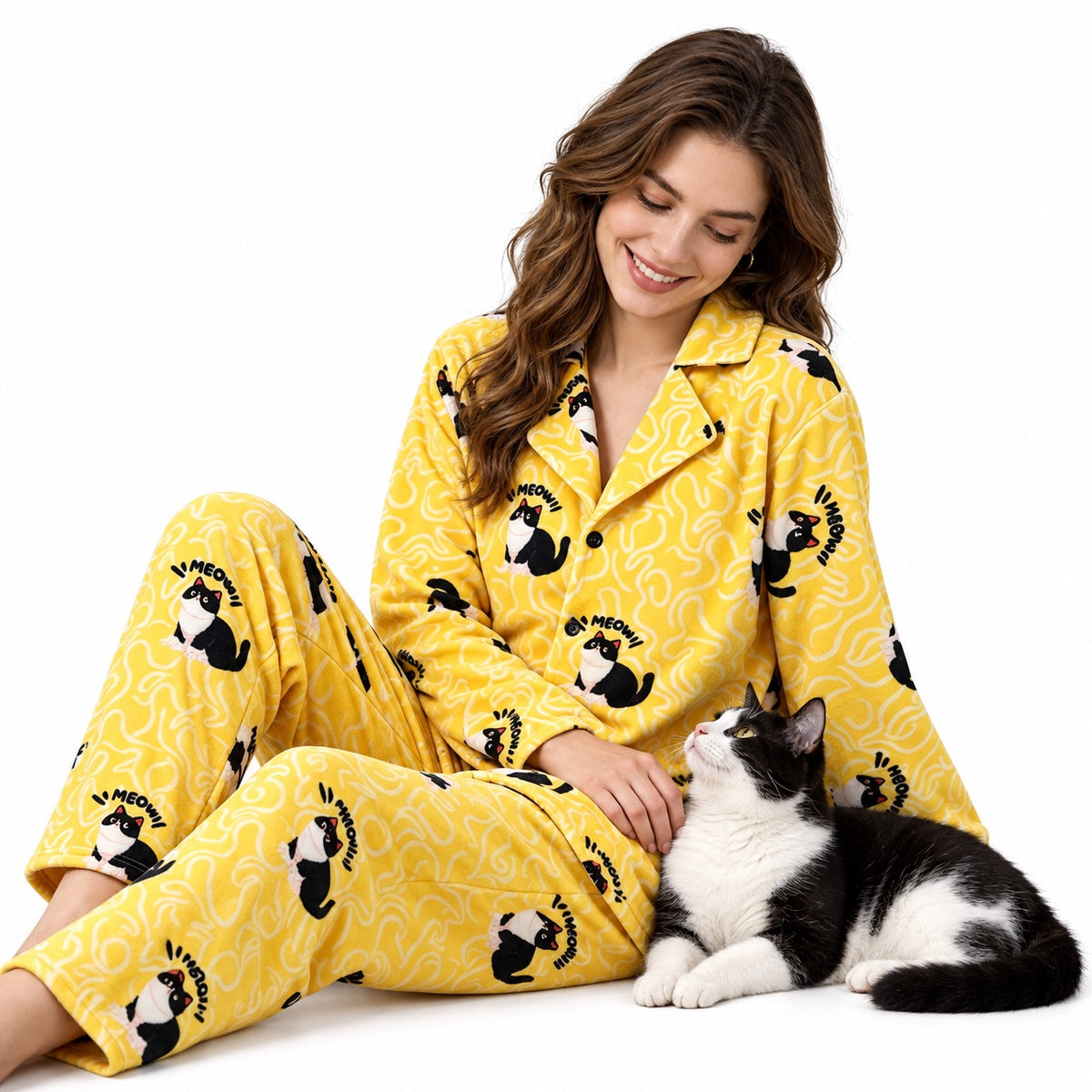 Person wearing yellow cat portrait pajamas, seated beside a tuxedo cat on a white background