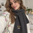 Woman wearing a gray knit scarf embroidered with a tabby cat portrait near the ribbed end