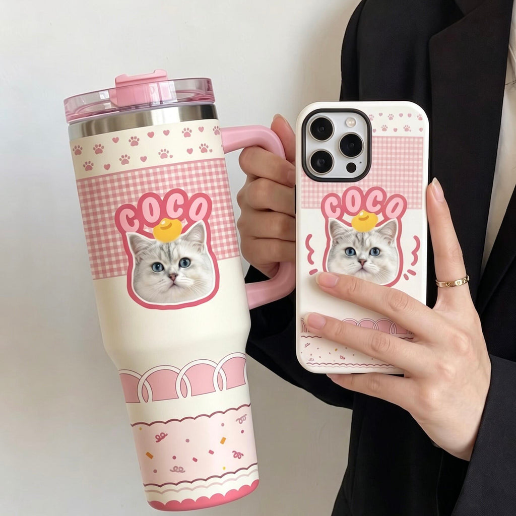 A close-up of a person holding a custom-designed travel tumbler and matching phone case, featuring a personalized cat illustration with the name COCO on a pink checkered background.