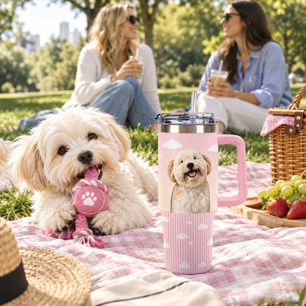 Small cream dog with a rope toy beside a custom dog photo tumbler on a pink picnic blanket