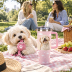 Small cream dog with a rope toy beside a custom dog photo tumbler on a pink picnic blanket