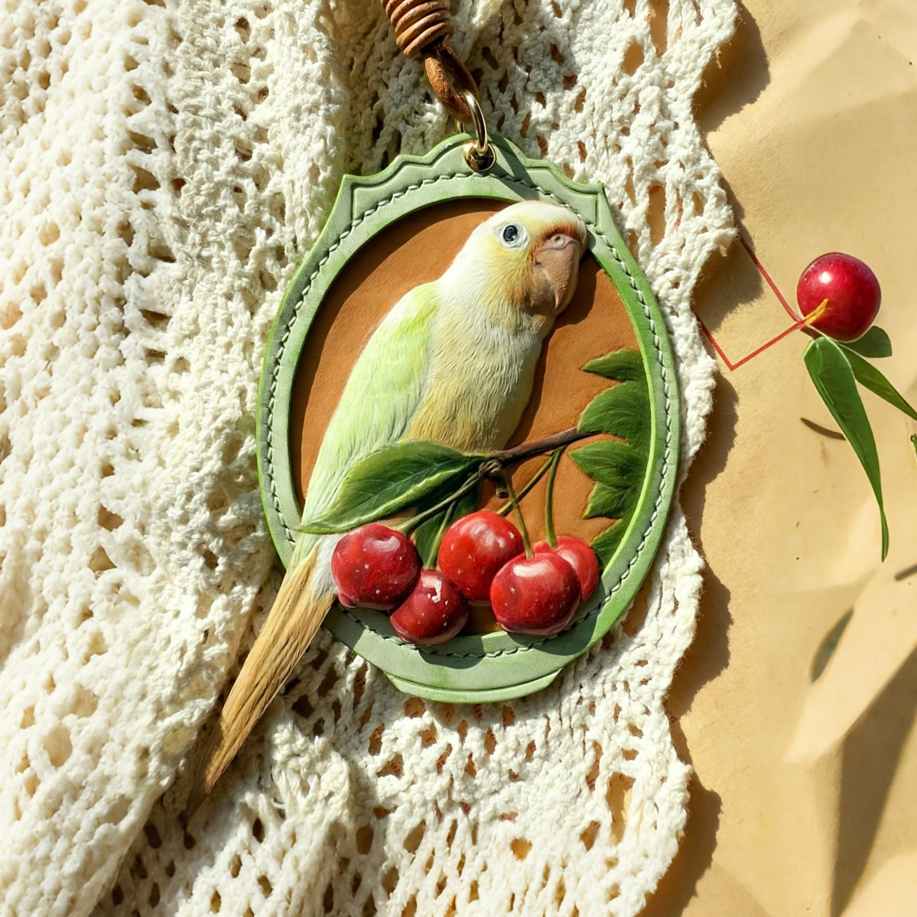 A hand-carved 3D leather parrot keychain featuring a realistic green and yellow parakeet portrait with red cherries, showcasing a premium personalized leather pet bird bag charm.