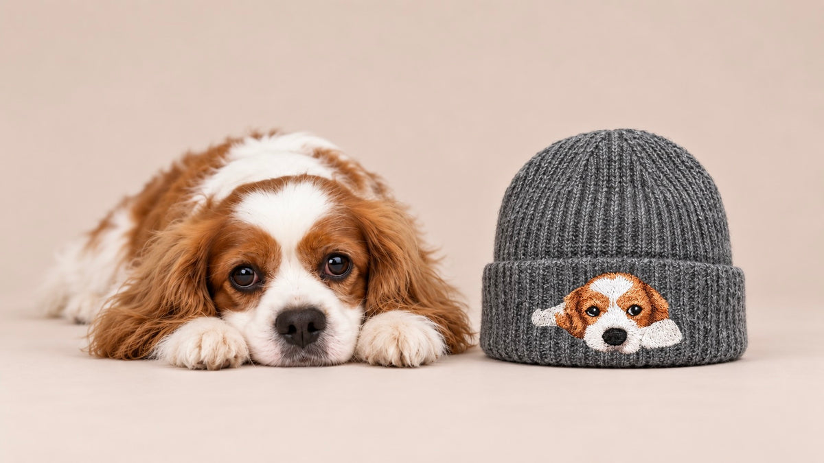 Personalized gray knit beanie embroidered with a Cavalier King Charles Spaniel portrait, displayed beside the matching brown and white dog.