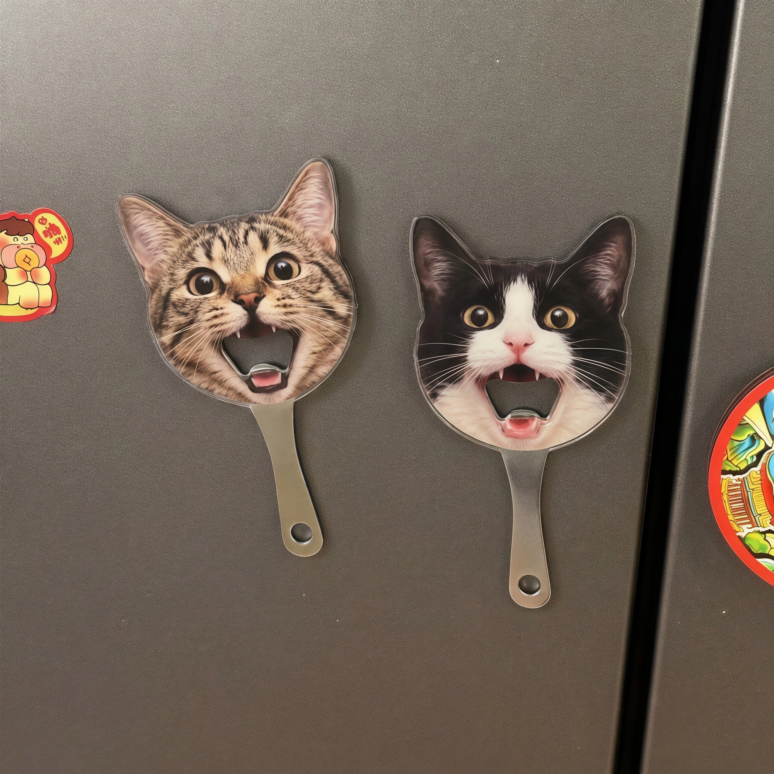 Two personalized pet photo magnetic bottle openers shaped like cat faces stuck securely onto a stainless steel refrigerator door.