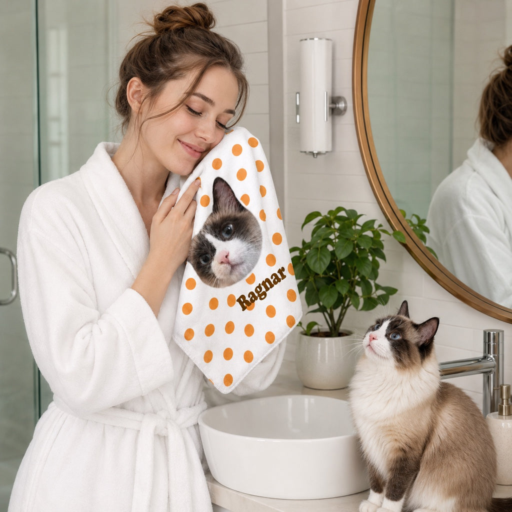 Woman holding a custom cat photo hand towel to her cheek in a bathroom while her cat sits nearby