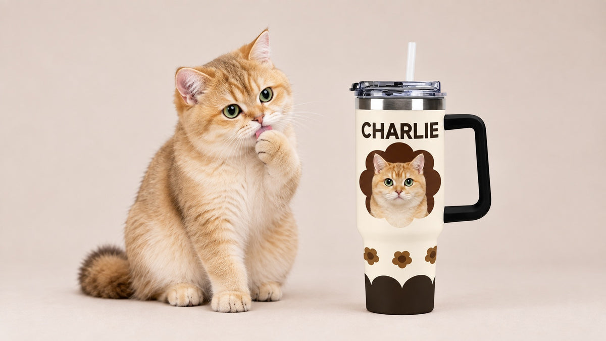 Golden British Shorthair cat licking its paw beside a personalized pet photo tumbler featuring its portrait and the name Charlie.