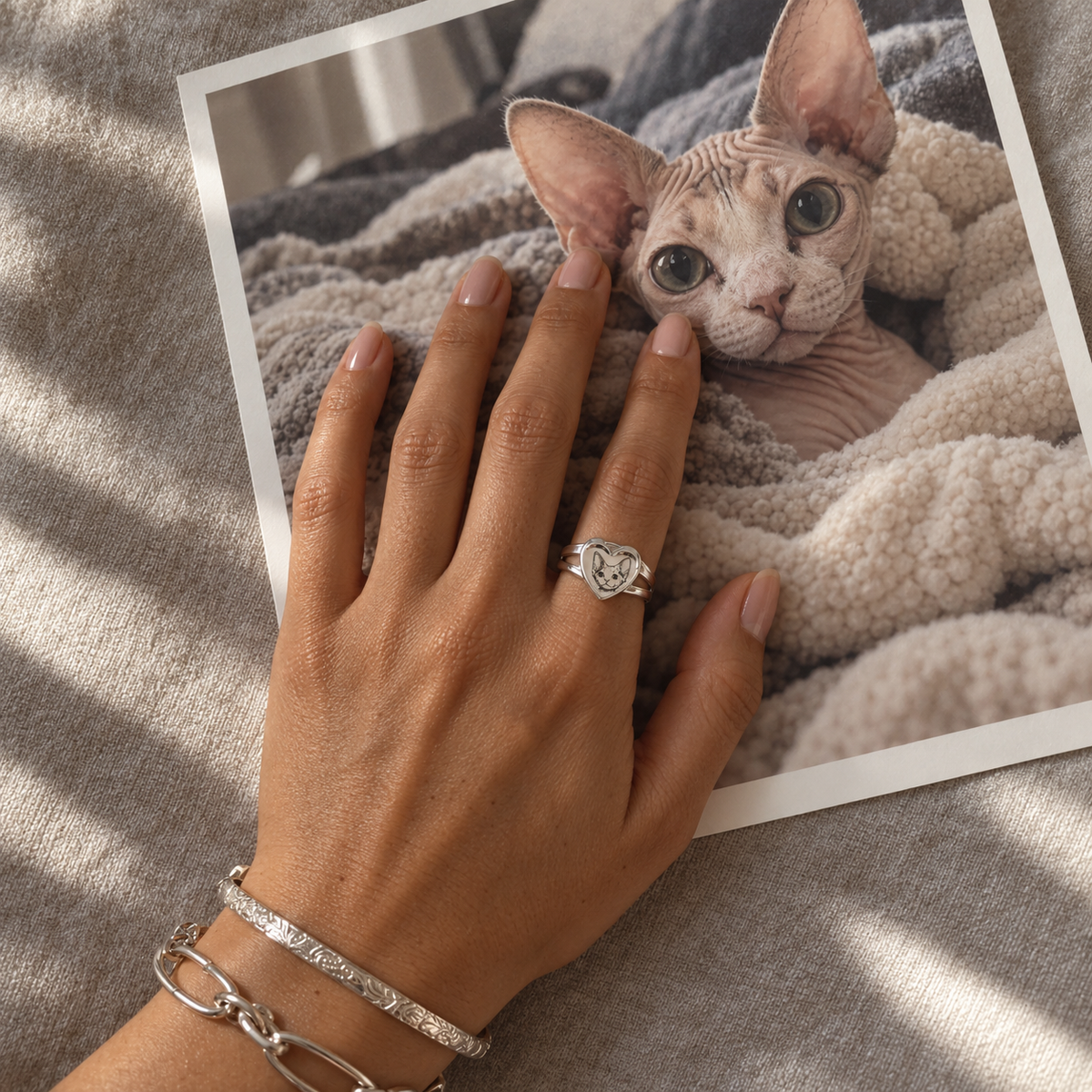 Hand wearing a personalized silver heart ring with a cat portrait placed on top of a printed photo of a Sphynx cat