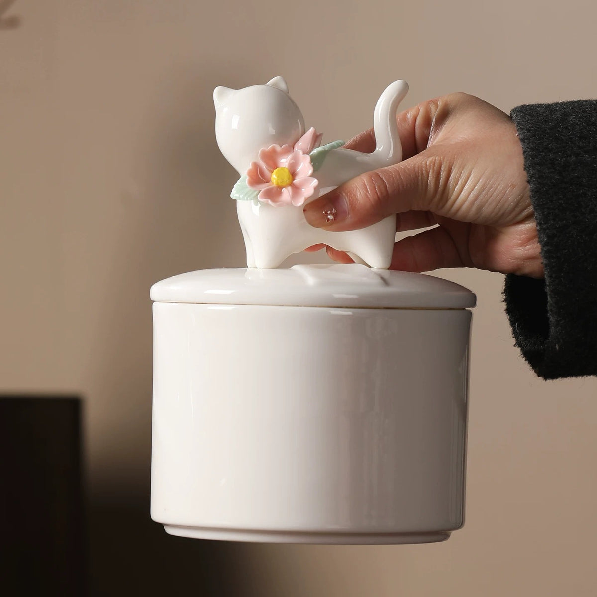 Hand lifting the cat-shaped floral lid from a large ivory ceramic cat memorial urn