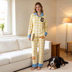 Person wearing yellow gingham dog portrait pajamas with blue trim beside a tricolor dog