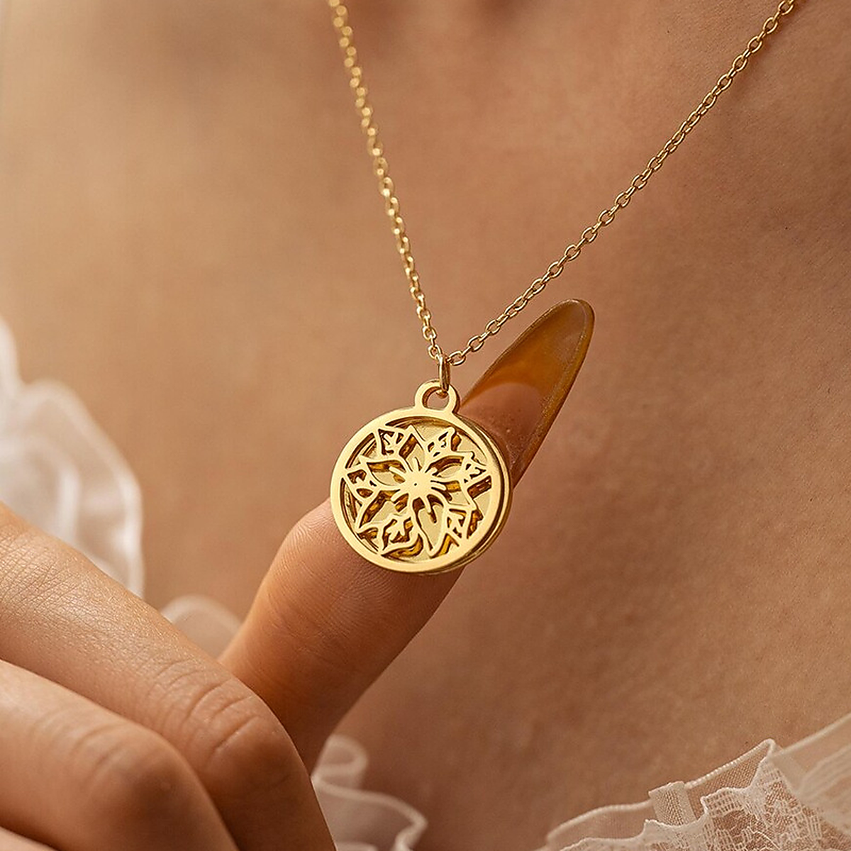 Close-up of a gold-tone openwork birth flower pendant held between two fingers