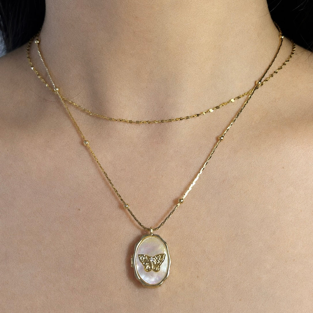 Model wearing a double-layered gold chain necklace featuring a custom oval locket pendant with a detailed gold butterfly design.