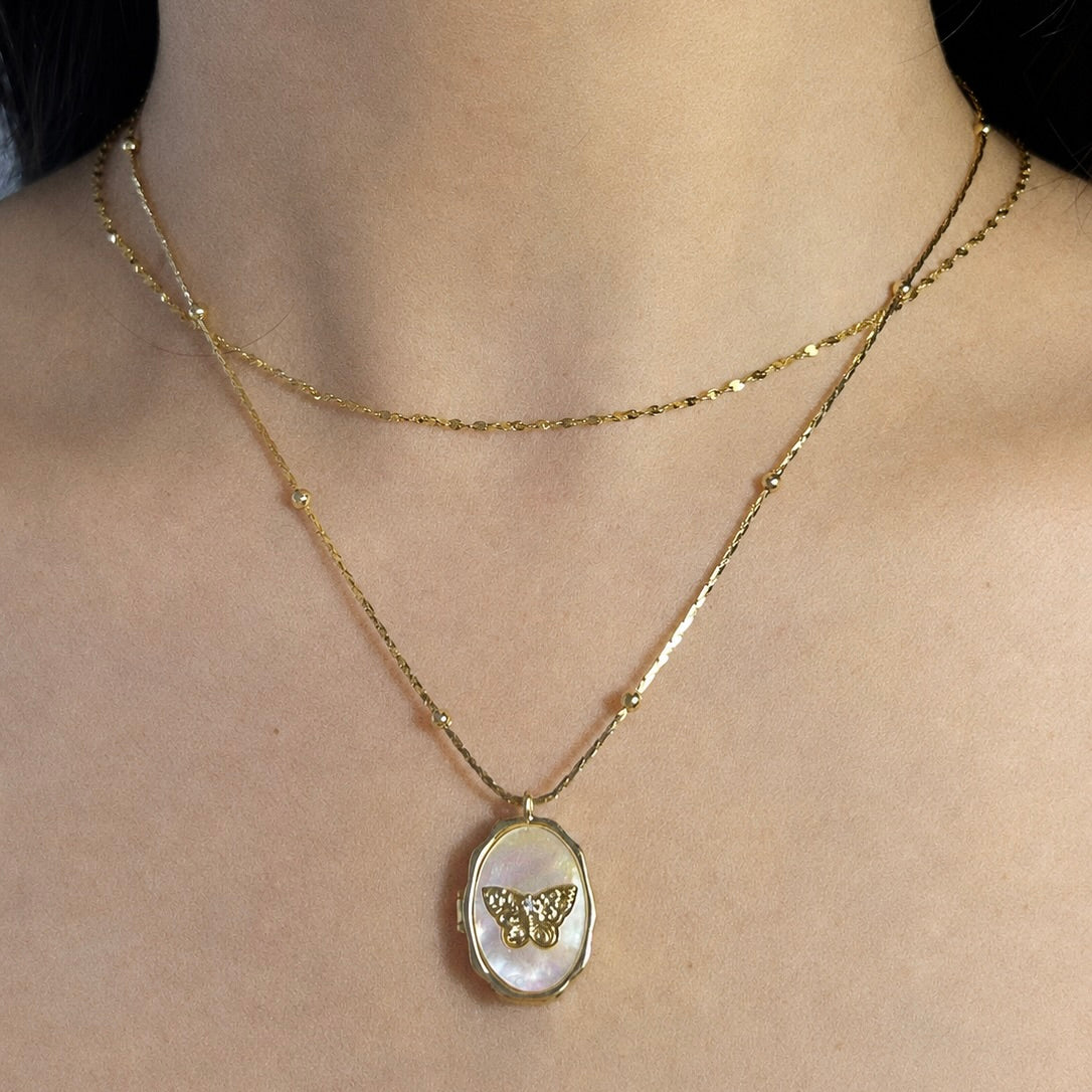Model wearing a double-layered gold chain necklace featuring a custom oval locket pendant with a detailed gold butterfly design.