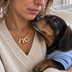 Woman wearing a gold custom pet portrait urn necklace with an engraved dog medallion, a miniature ashes capsule, and an angel wing charm
