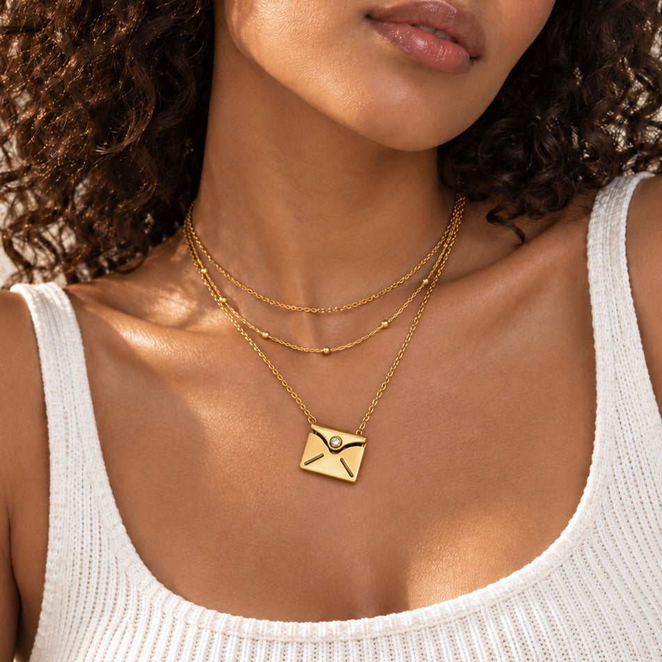 Model wearing a closed gold envelope pendant necklace layered with two delicate chains