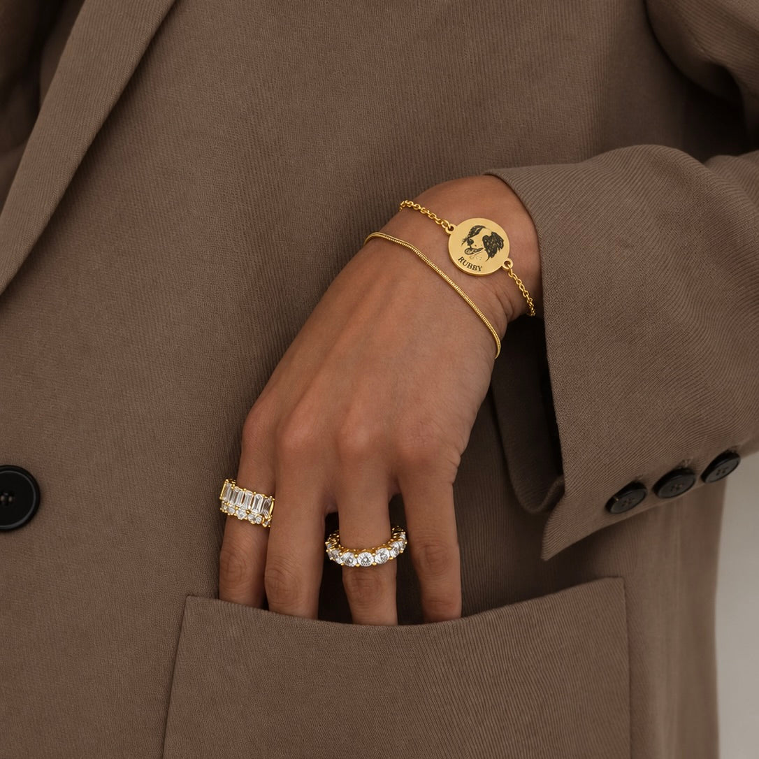 Gold layered bracelet with a custom dog portrait and short name worn with a brown jacket