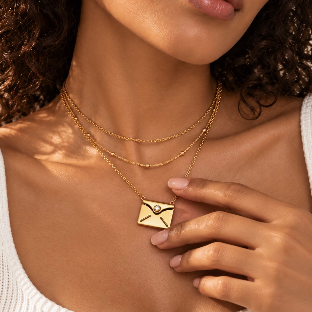 Close view of a model touching a closed gold personalized envelope necklace