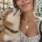 Close-up of a model wearing a gold pendant necklace with a custom pet photo inside, lovingly hugging a Shiba Inu dog outdoors